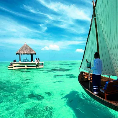 Luxury boat sailing across crystal-clear turquoise waters in the Maldives near a private overwater pavilion