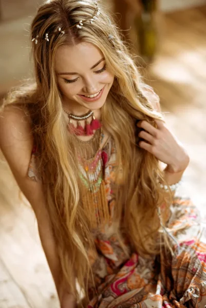 Smiling blonde woman with long hair wearing a bohemian dress and colorful necklace indoors