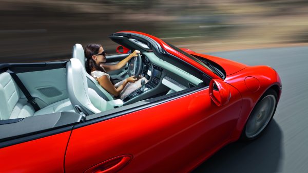 Woman driving a red convertible sports car on a scenic road, viewed from above — luxury lifestyle and fast travel concept.