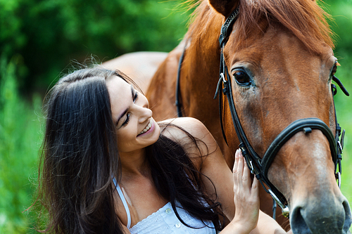 woman gently holding a brown horse’s head outdoors, close-up shot