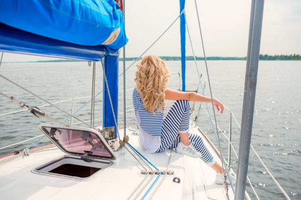 woman in striped summer suit sits on bow of yacht and looks at sea