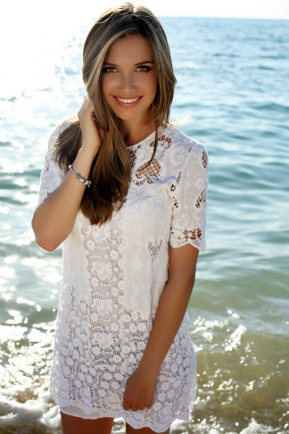 young woman in white summer dress standing in shallow sea water smiling