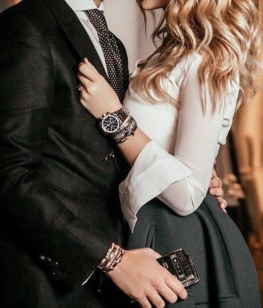 blonde girl in white skirt holds jacket cuff of elegant man standing next to her