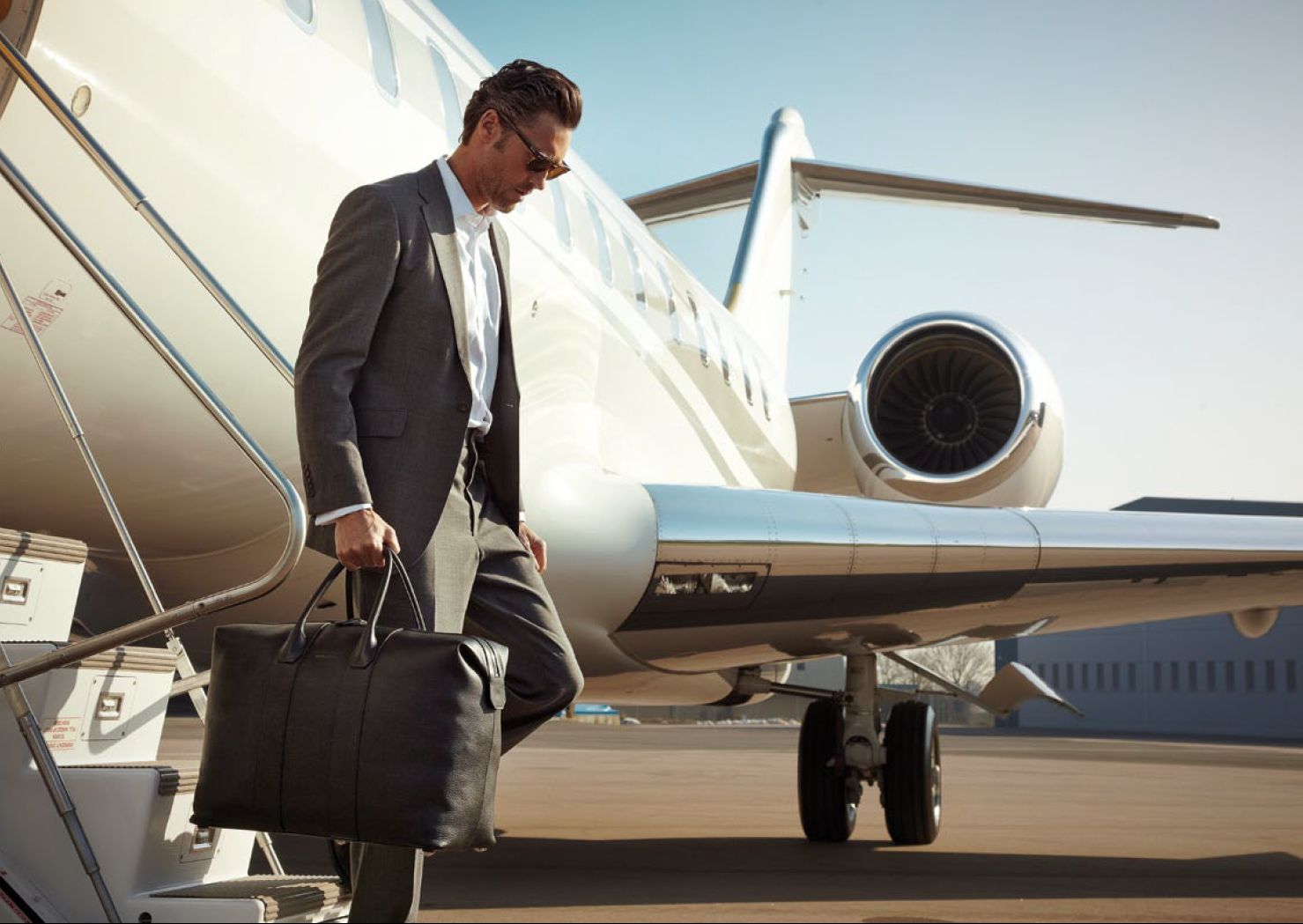 man walking in airport terminal pulling the bag, private jet behind him